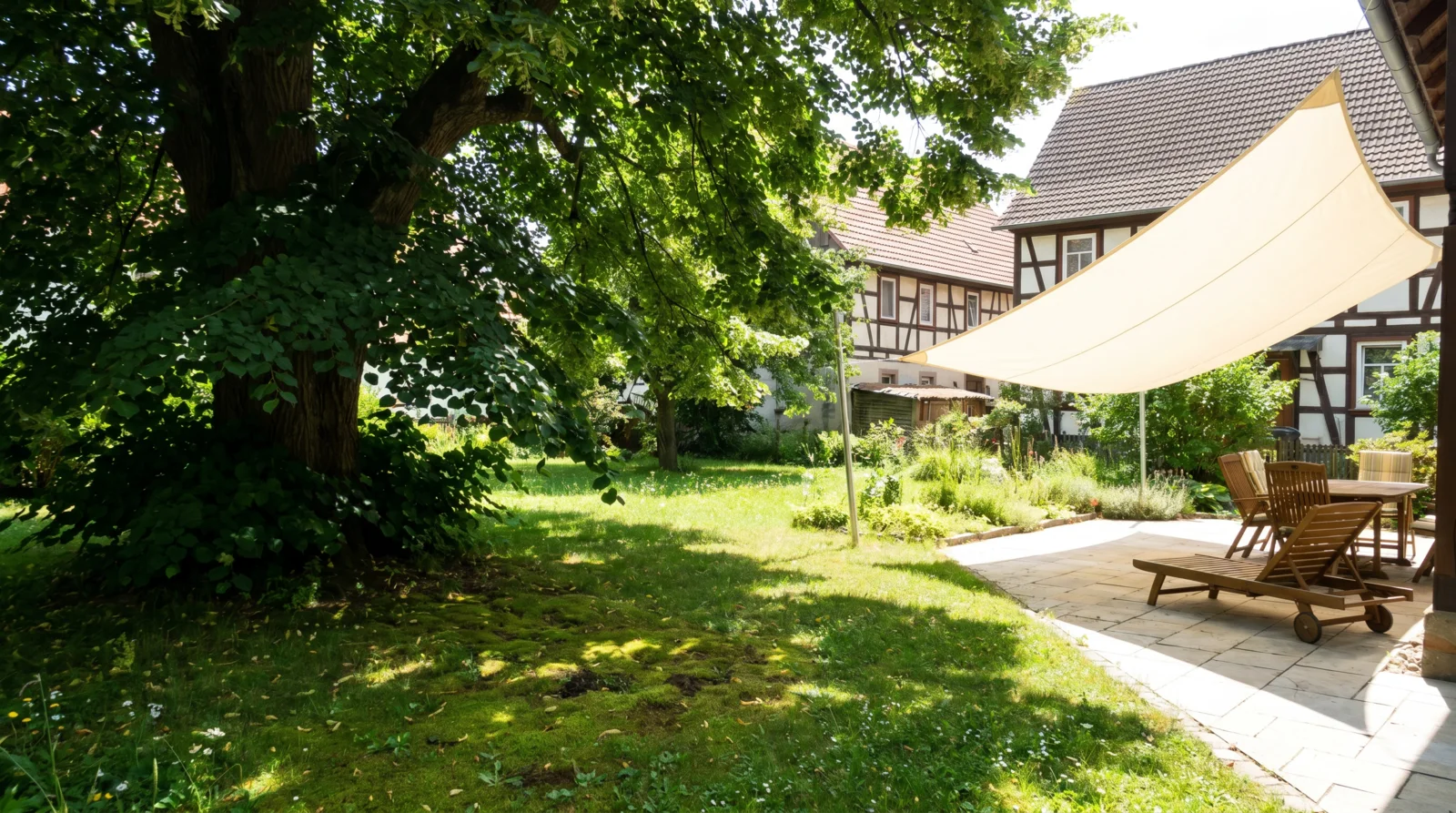 Vergleich im Garten: links tiefer Baumschatten unter einer Linde, rechts ein helles Sonnensegel über einer Steinterrasse